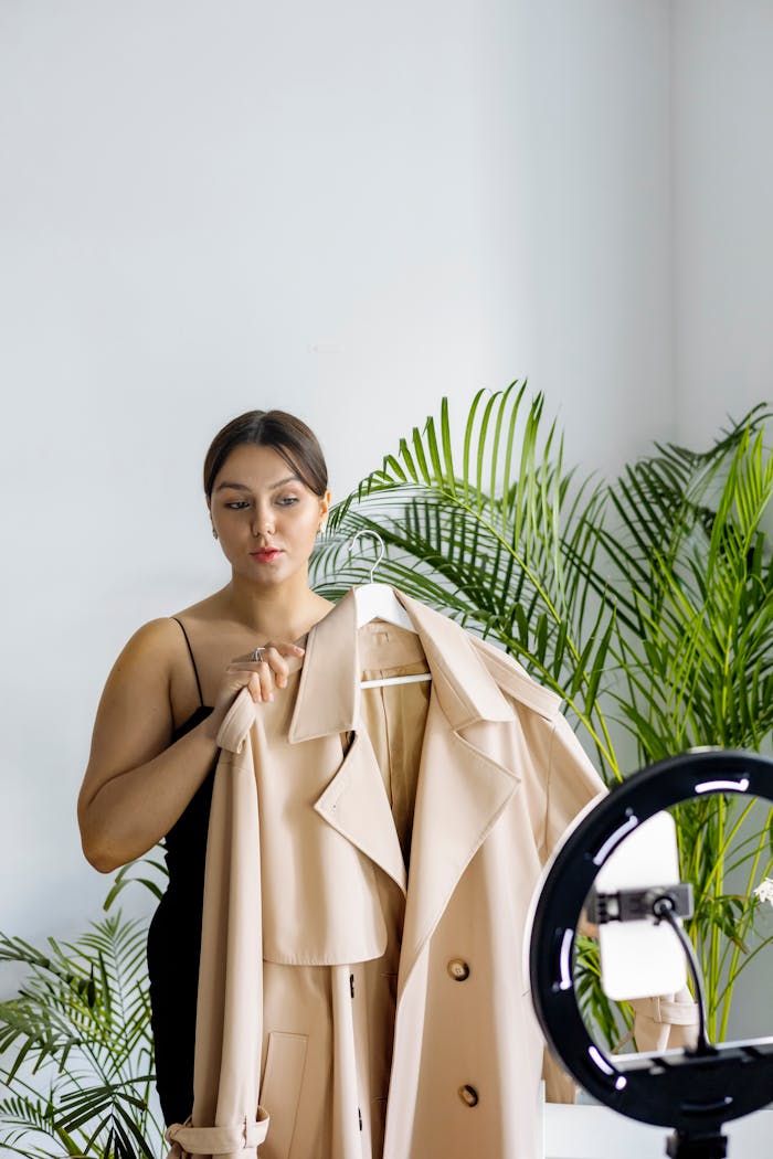 about-01 A fashion vlogger presents a chic beige coat during an indoor recording session with ring light.